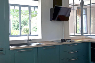 Diseño de cocinas en U contemporáneo con puertas de armario verdes, encimera de madera, electrodomésticos negros y suelo de terrazo