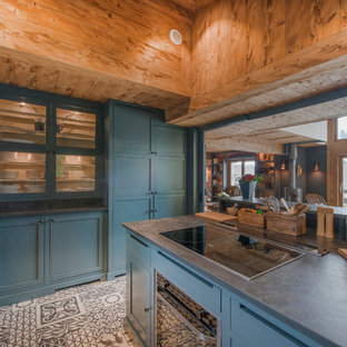 Inspiration pour une cuisine ouverte chalet en L avec un placard à porte vitrée, des portes de placard bleues, une crédence grise, un électroménager noir, un îlot central et un sol multicolore.