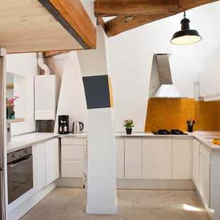 Cette image montre une cuisine design en U fermée et de taille moyenne avec des portes de placard blanches, aucun îlot et une crédence orange.