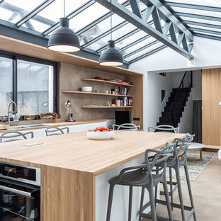 Idée de décoration pour une cuisine américaine linéaire urbaine de taille moyenne avec un plan de travail en bois, un îlot central, un plan de travail beige, un évier 2 bacs, un placard à porte plane, des portes de placard blanches, une crédence marron, un électroménager en acier inoxydable et un sol marron.