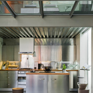 Idee per una cucina industriale di medie dimensioni con ante lisce, ante in acciaio inossidabile, paraspruzzi a effetto metallico, elettrodomestici in acciaio inossidabile e isola