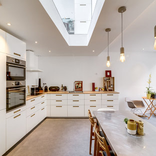 Exemple d'une grand cuisine américaine tendance en L avec un électroménager en acier inoxydable, un évier 2 bacs, un placard à porte affleurante, des portes de placard bleues, un plan de travail en bois, un sol en vinyl, un sol gris, aucun îlot et une crédence blanche.