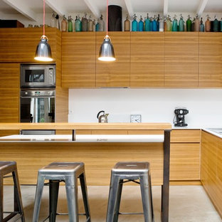 Réalisation d'une cuisine américaine design en L de taille moyenne avec un îlot central, un évier encastré, un placard à porte affleurante, des portes de placard en bois brun, un plan de travail en quartz modifié, une crédence blanche, un électroménager encastrable et béton au sol.