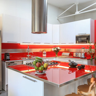 Aménagement d'une grand cuisine contemporaine en L avec un évier encastré, des portes de placard blanches, un plan de travail en verre, une crédence rouge, un électroménager en acier inoxydable, béton au sol, un îlot central, un sol gris, un plan de travail rouge, un placard à porte plane et une crédence en feuille de verre.