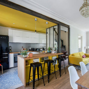 Small contemporary u-shaped open plan kitchen in Paris with a double-bowl sink, beaded inset cabinets, white cabinets, wood benchtops, grey splashback, metal splashback, black appliances, cement tiles, with island and multi-coloured floor.