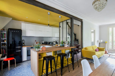 Exempel på ett litet modernt kök, med en dubbel diskho, luckor med profilerade fronter, vita skåp, träbänkskiva, grått stänkskydd, stänkskydd i metallkakel, svarta vitvaror, cementgolv, en köksö och flerfärgat golv