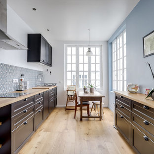 Exemple d'une cuisine américaine parallèle chic avec un placard avec porte à panneau encastré, des portes de placard noires, un plan de travail en bois, une crédence multicolore, un sol en bois clair, un sol beige et un plan de travail beige.