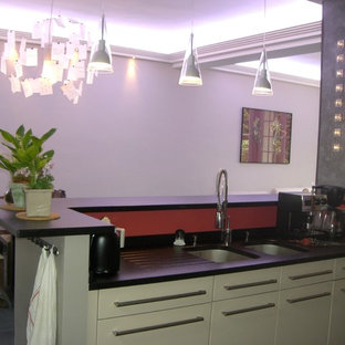 Photo of a mid-sized contemporary l-shaped open plan kitchen in Paris with a double-bowl sink, black floor, flat-panel cabinets, beige cabinets, granite benchtops, red splashback, stainless steel appliances, ceramic floors and no island.