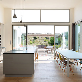 Idées déco pour une grand cuisine américaine parallèle contemporaine avec un évier encastré, un placard à porte plane, des portes de placard grises, un sol en bois clair, un îlot central et une crédence blanche.