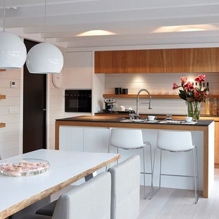 Réalisation d'une grand cuisine américaine parallèle vintage avec un placard à porte plane, des portes de placard en bois brun, un électroménager en acier inoxydable, un sol en bois clair et un îlot central.