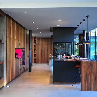 Idée de décoration pour une grand cuisine ouverte linéaire design avec des portes de placard en bois sombre, un plan de travail en bois, béton au sol et un îlot central.
