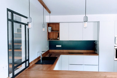 Réalisation d'une cuisine américaine design en U avec des portes de placard blanches, un plan de travail en bois, une crédence en bois, un électroménager blanc et sol en béton ciré.