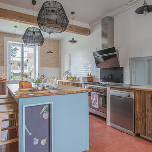 Aménagement d'une cuisine campagne en L avec un évier posé, un placard à porte plane, des portes de placard en bois brun, un plan de travail en bois, un îlot central, un sol rouge et un plan de travail marron.