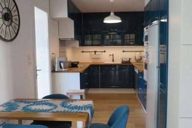 Foto på ett mellanstort vintage kök, med en undermonterad diskho, luckor med upphöjd panel, blå skåp, träbänkskiva, vitt stänkskydd, vita vitvaror och ljust trägolv