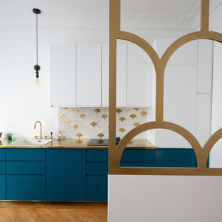 This is an example of a mid-sized scandinavian galley open plan kitchen in Paris with a single-bowl sink, beaded inset cabinets, blue cabinets, copper benchtops, white splashback, ceramic splashback, black appliances, light hardwood floors, no island, brown floor and yellow benchtop.