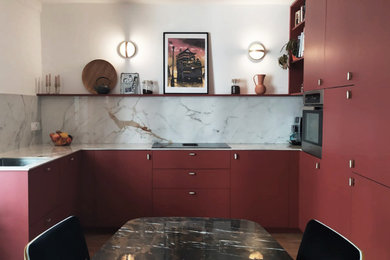 Cette image montre une cuisine encastrable design en U de taille moyenne avec un évier encastré, un placard à porte plane, des portes de placard rouges, une crédence grise, un sol marron et un plan de travail gris.