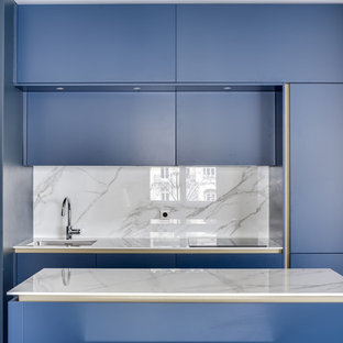 Cette photo montre une cuisine linéaire tendance avec un évier encastré, un placard à porte plane, des portes de placard bleues, une crédence grise, un îlot central et un plan de travail gris.