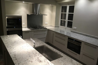 Cette photo montre une cuisine chic avec un évier intégré, un plan de travail en granite, un électroménager en acier inoxydable et tomettes au sol.