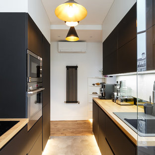 Inspiration pour une cuisine parallèle design avec un évier posé, un placard à porte plane, des portes de placard noires, un plan de travail en bois, une crédence noire, un électroménager noir, un sol en bois brun, un sol marron et un plan de travail beige.