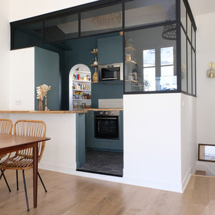 Cette photo montre une cuisine ouverte industrielle en L de taille moyenne avec des portes de placards vertess, un plan de travail en bois, un électroménager en acier inoxydable, un sol en carrelage de céramique, un sol noir, un évier 1 bac, une crédence beige, une crédence en carreau de terre cuite, un îlot central et un plan de travail beige.