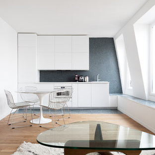 Idées déco pour une petit cuisine ouverte linéaire contemporaine avec un placard à porte plane, des portes de placard blanches, une crédence noire, une crédence en mosaïque, un électroménager en acier inoxydable, un sol en bois clair, un évier encastré et aucun îlot.