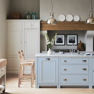 Exemple d'une cuisine parallèle chic avec un placard avec porte à panneau encastré, des portes de placard blanches, un sol en bois clair, un îlot central, un sol beige et un plan de travail blanc.