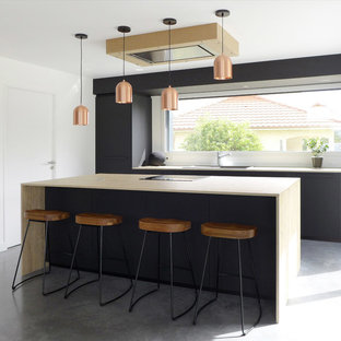 Cette image montre une cuisine parallèle design de taille moyenne avec un évier posé, un placard à porte plane, des portes de placard noires, un plan de travail en bois, une crédence en fenêtre, béton au sol, un îlot central, un sol gris et un plan de travail marron.