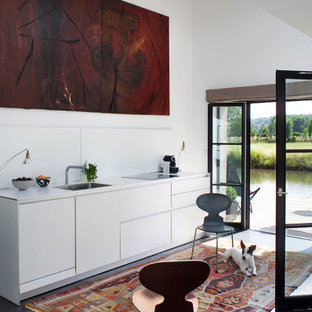 Idées déco pour une cuisine ouverte linéaire contemporaine avec des portes de placard blanches, une crédence blanche, un sol en ardoise, un sol noir, un plan de travail blanc, un évier encastré, un placard à porte plane, aucun îlot et un plafond voûté.
