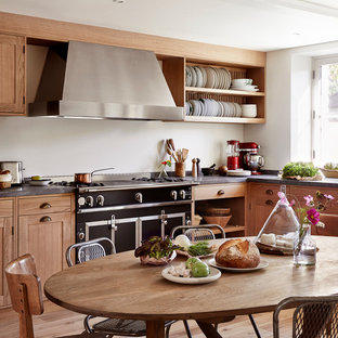 Cette photo montre une cuisine américaine nature en L de taille moyenne avec un placard à porte shaker, des portes de placard en bois brun, un électroménager noir, aucun îlot, une crédence blanche et un sol en bois brun.
