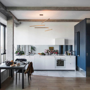 Réalisation d'une cuisine linéaire design avec un évier encastré, un placard à porte plane, des portes de placard blanches, une crédence métallisée, une crédence en carreau de miroir, un électroménager blanc, un sol en bois brun, un sol marron et un plan de travail blanc.