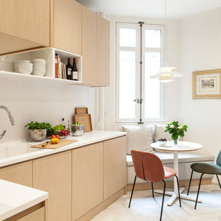 Idée de décoration pour une cuisine américaine design en L avec un évier intégré, un placard à porte plane, des portes de placard en bois clair, une crédence blanche et un sol beige.