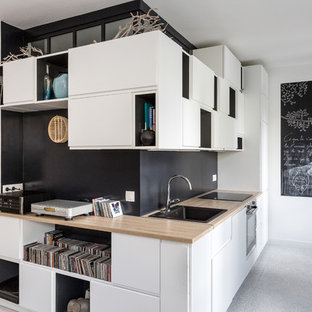 Design ideas for a mid-sized modern single-wall open plan kitchen in Paris with wood benchtops, a drop-in sink, flat-panel cabinets, white cabinets, black splashback, slate splashback, black appliances, vinyl floors, no island, grey floor and beige benchtop.