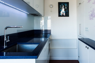 パリにある低価格の小さなコンテンポラリースタイルのおしゃれなキッチン (シングルシンク、インセット扉のキャビネット、白いキャビネット、珪岩カウンター、白いキッチンパネル、ガラス板のキッチンパネル、シルバーの調理設備、無垢フローリング、アイランドなし、茶色い床、青いキッチンカウンター) の写真