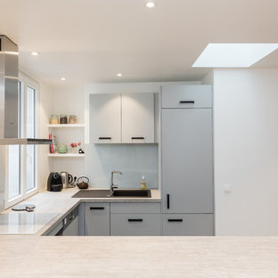 Mid-sized eclectic u-shaped open plan kitchen in Paris with no island, a drop-in sink, flat-panel cabinets, grey cabinets, laminate benchtops, white splashback, glass sheet splashback, stainless steel appliances, ceramic floors, grey floor and grey benchtop.