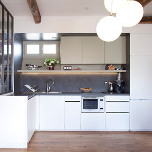 Réalisation d'une cuisine ouverte design en L de taille moyenne avec un évier 2 bacs, un placard à porte plane, des portes de placard blanches, une crédence grise, un électroménager blanc, un sol en bois brun et une péninsule.