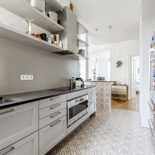 Cette photo montre une cuisine parallèle tendance fermée et de taille moyenne avec un évier encastré, des portes de placard blanches, une crédence grise, un électroménager encastrable, un sol en carrelage de céramique et aucun îlot.