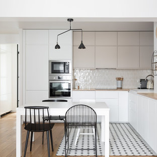 Réalisation d'une cuisine ouverte design en L de taille moyenne avec un placard à porte plane, des portes de placard blanches, un plan de travail en bois, une crédence beige, une crédence en carreau de porcelaine, un électroménager encastrable, un sol en carrelage de porcelaine, aucun îlot, un plan de travail beige, un évier posé et un sol multicolore.