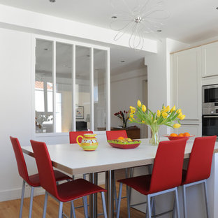 Idée de décoration pour une cuisine design en L fermée et de taille moyenne avec des portes de placard blanches, un sol en bois clair et un îlot central.