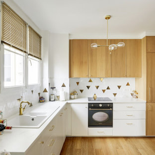 Idée de décoration pour une cuisine design en L de taille moyenne avec un évier posé, un placard à porte plane, des portes de placard blanches, une crédence multicolore, un électroménager encastrable, un sol en bois brun, un sol beige et un plan de travail blanc.