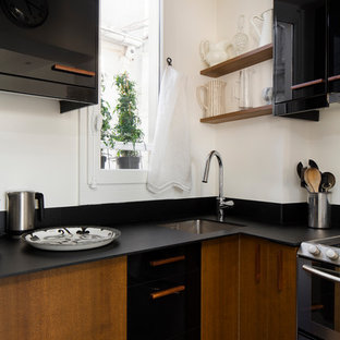 Inspiration pour une cuisine design en L avec un évier encastré, un placard à porte plane, des portes de placard noires et un plan de travail noir.