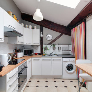 Cette photo montre une cuisine tendance en L avec un évier intégré, un placard à porte plane, des portes de placard blanches, un plan de travail en bois, une crédence blanche, un électroménager blanc, un sol beige, un plan de travail marron et un plafond voûté.