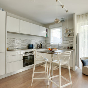 Cette image montre une petit cuisine américaine traditionnelle en U avec un évier 1 bac, un placard à porte shaker, des portes de placard blanches, un plan de travail en stratifié, une crédence beige, une crédence en carreau de céramique, un électroménager encastrable, sol en stratifié, un îlot central, un sol marron et un plan de travail marron.