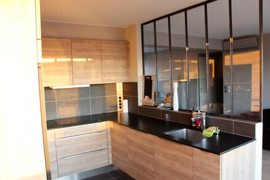 This is an example of a contemporary u-shaped open plan kitchen in Paris with a single-bowl sink, flat-panel cabinets, light wood cabinets, granite worktops, grey splashback, ceramic splashback, black appliances and ceramic flooring.