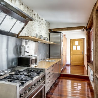 Aménagement d'une grand cuisine linéaire contemporaine fermée avec un évier posé, un placard à porte plane, une façade en inox, un plan de travail en bois, une crédence métallisée, un électroménager en acier inoxydable, un sol en bois brun et aucun îlot.