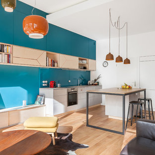 Aménagement d'une cuisine ouverte linéaire contemporaine avec un évier encastré, un placard à porte plane, des portes de placard grises, un plan de travail en bois, une crédence bleue, une crédence en feuille de verre, un électroménager en acier inoxydable, un sol en bois brun, un îlot central, un sol marron et un plan de travail marron.
