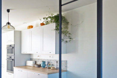 Exemple d'une cuisine blanche et bois avec des portes de placard blanches, un plan de travail en bois, une crédence bleue, une crédence en carreau de ciment et un sol gris.