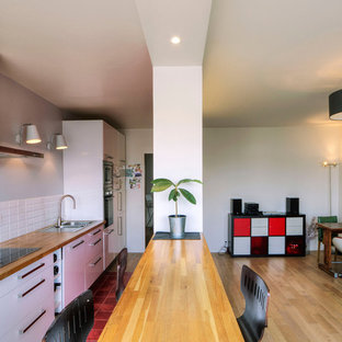 Cette photo montre une grand cuisine ouverte linéaire tendance avec un évier posé, un placard à porte plane, des portes de placard blanches, un plan de travail en bois, une crédence blanche, un sol en bois brun et une péninsule.