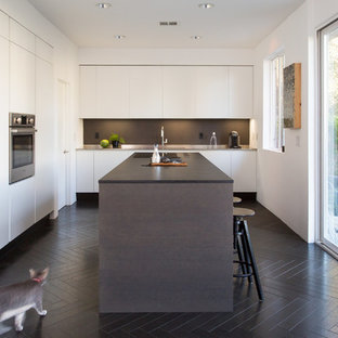 Cette photo montre une cuisine tendance en L avec un placard à porte plane, des portes de placard blanches, une crédence noire, un électroménager en acier inoxydable, un îlot central, un sol noir et un plan de travail noir.