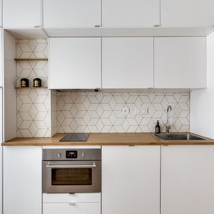 Réalisation d'une petit cuisine américaine linéaire nordique avec des portes de placard blanches, un plan de travail en bois, une crédence blanche, une crédence en carreau de céramique, un sol en bois clair, aucun îlot, un évier posé, un placard à porte plane et un électroménager en acier inoxydable.