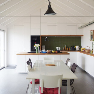 Réalisation d'une grand cuisine américaine design en L avec des portes de placard blanches, un plan de travail en bois, une crédence verte, une crédence en carreau de céramique, un électroménager noir, un sol en vinyl, un îlot central et un placard à porte plane.